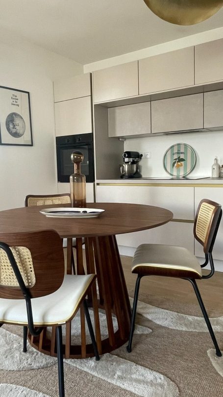 Table en bois avec chaises, cuisine moderne en arrière-plan et décor minimaliste.