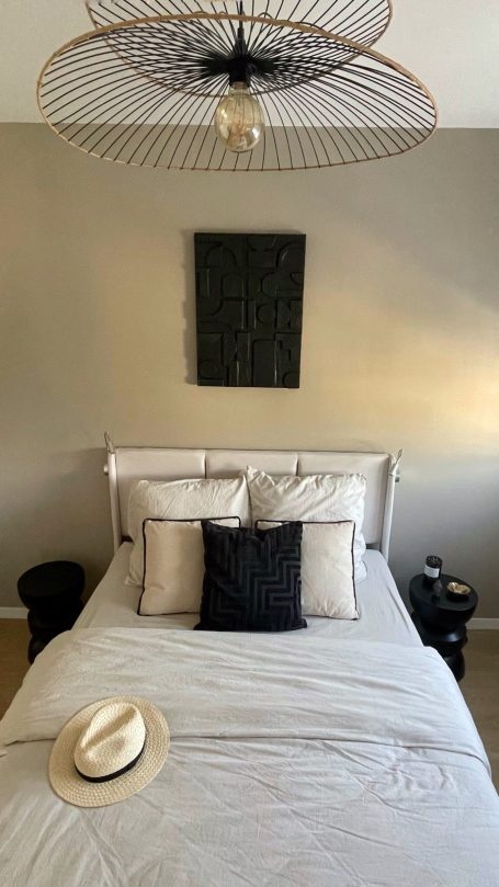 Lit de chambre avec coussins blancs et noirs, tableau abstrait au-dessus.